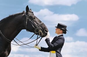 woman in dressage habit petting black horse