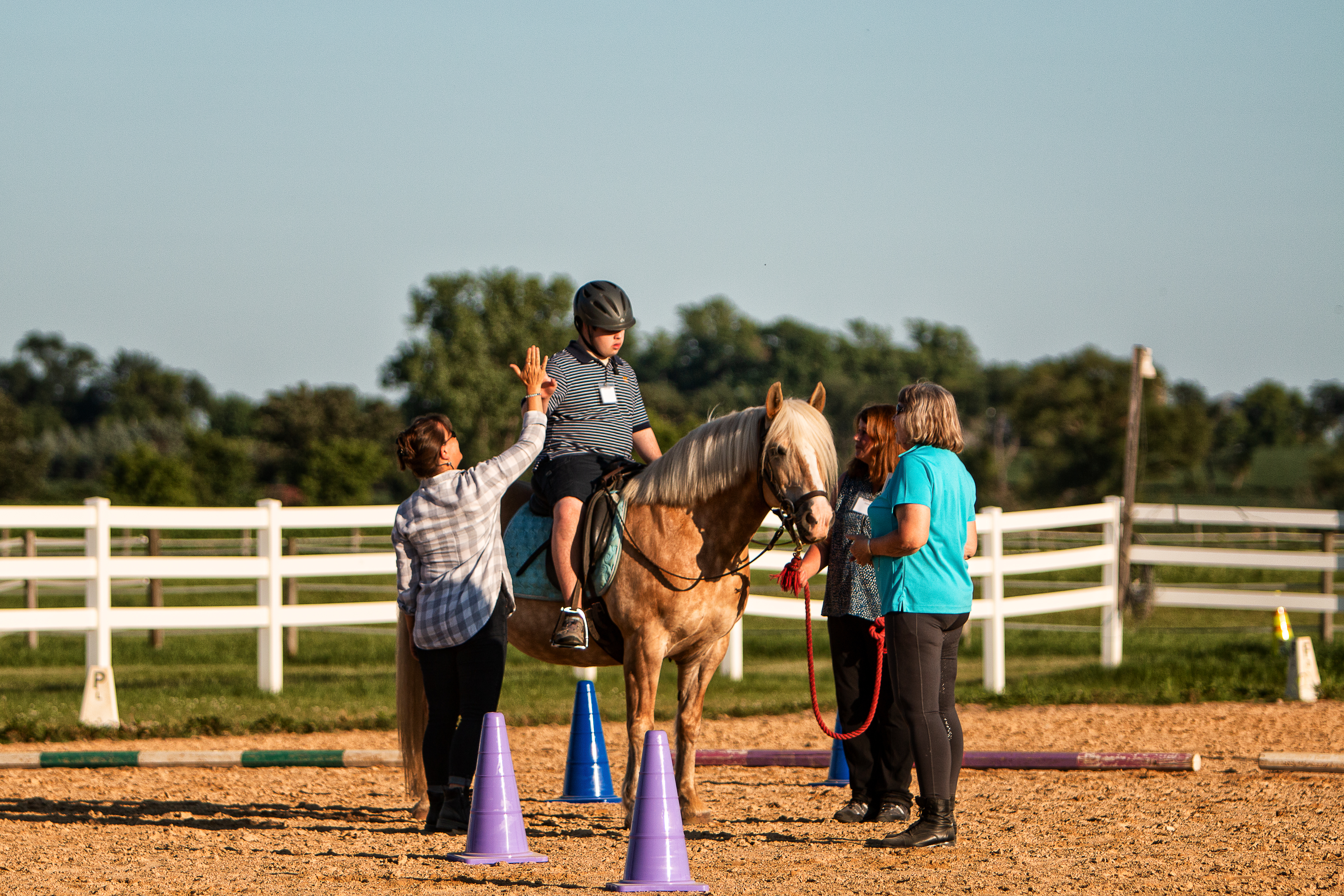 Child on horse high-fives instructor, outdoor setting.